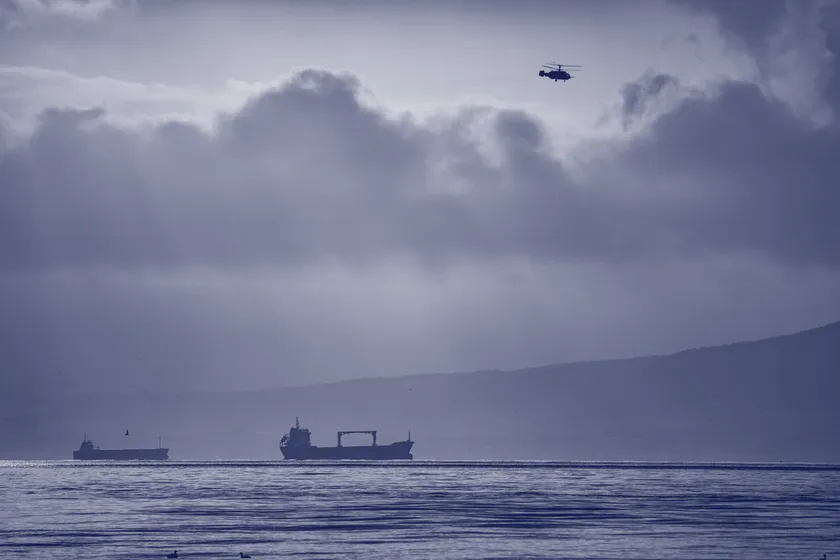 A helicopter over open sea with a cargo ship below — air and sea in one frame